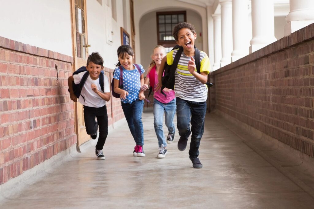 four kids running in the hallway of a school with brick wall on side