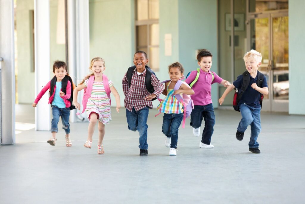 A bunch of kids running with their backpacks and smiling